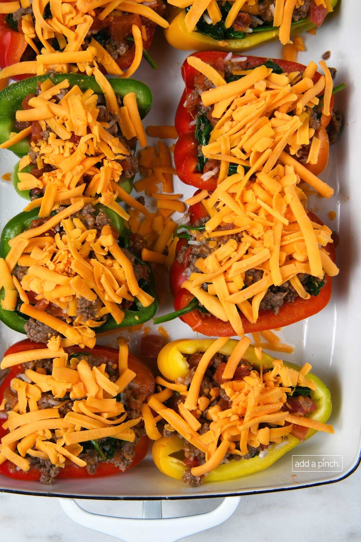 Shredded cheddar cheese tops bell peppers stuffed with meat mixture before baking.