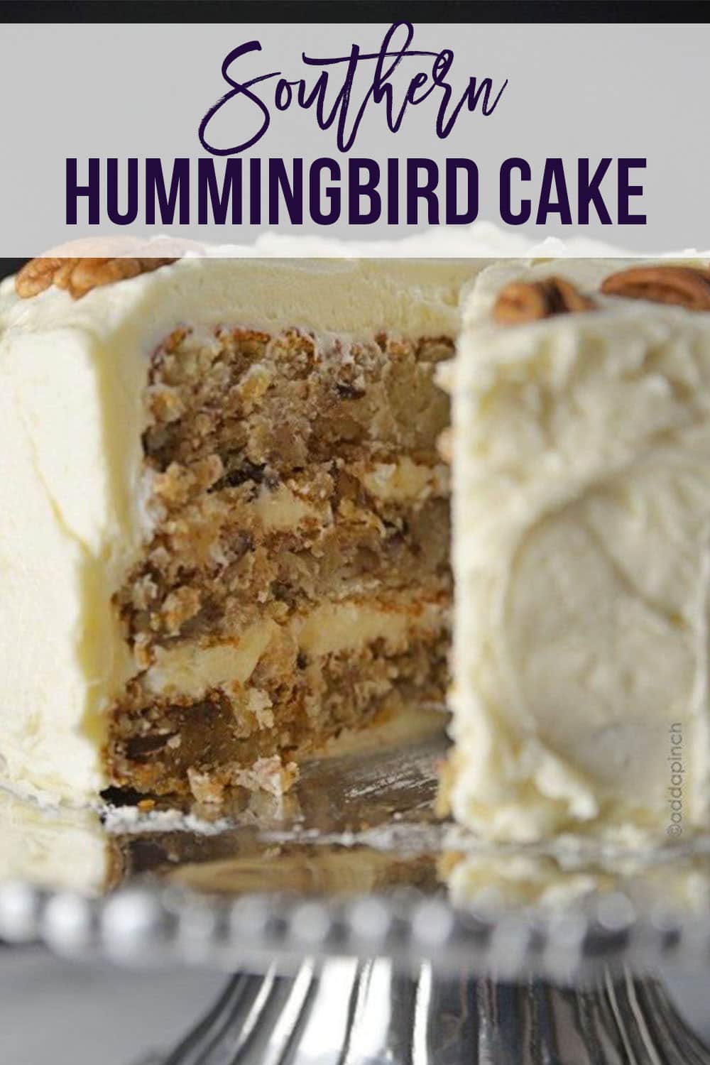 Closeup of Hummingbird Cake with cream cheese frosting topped with pecan halves - with text - addapinch.com