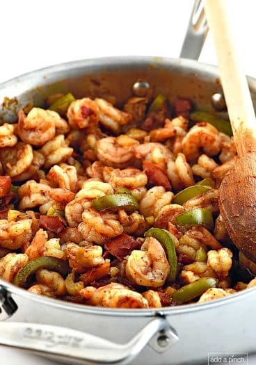Photo of Shrimp Creole with shrimp, green pepper slices and tomatoes with a wooden spoon in a stainless steel skillet