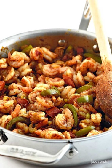 Photo of Shrimp Creole with shrimp, green pepper slices and tomatoes with a wooden spoon in a stainless steel skillet