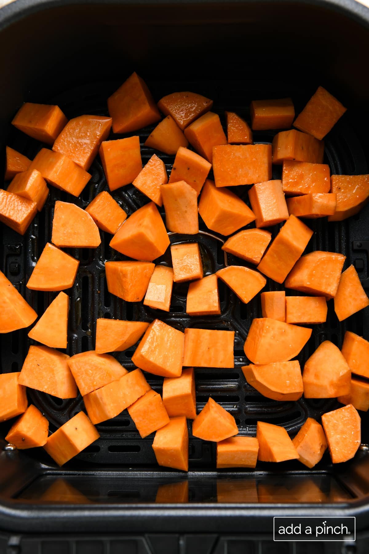 Seasoned sweet potato cubes in air fryer basket ready to be cooked.
