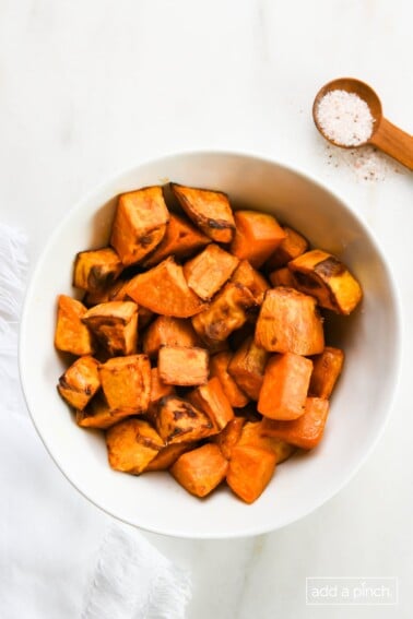 Roasted sweet potatoes in a white bowl on a marble surface.