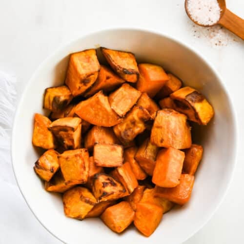 Roasted sweet potatoes in a white bowl on a marble surface.