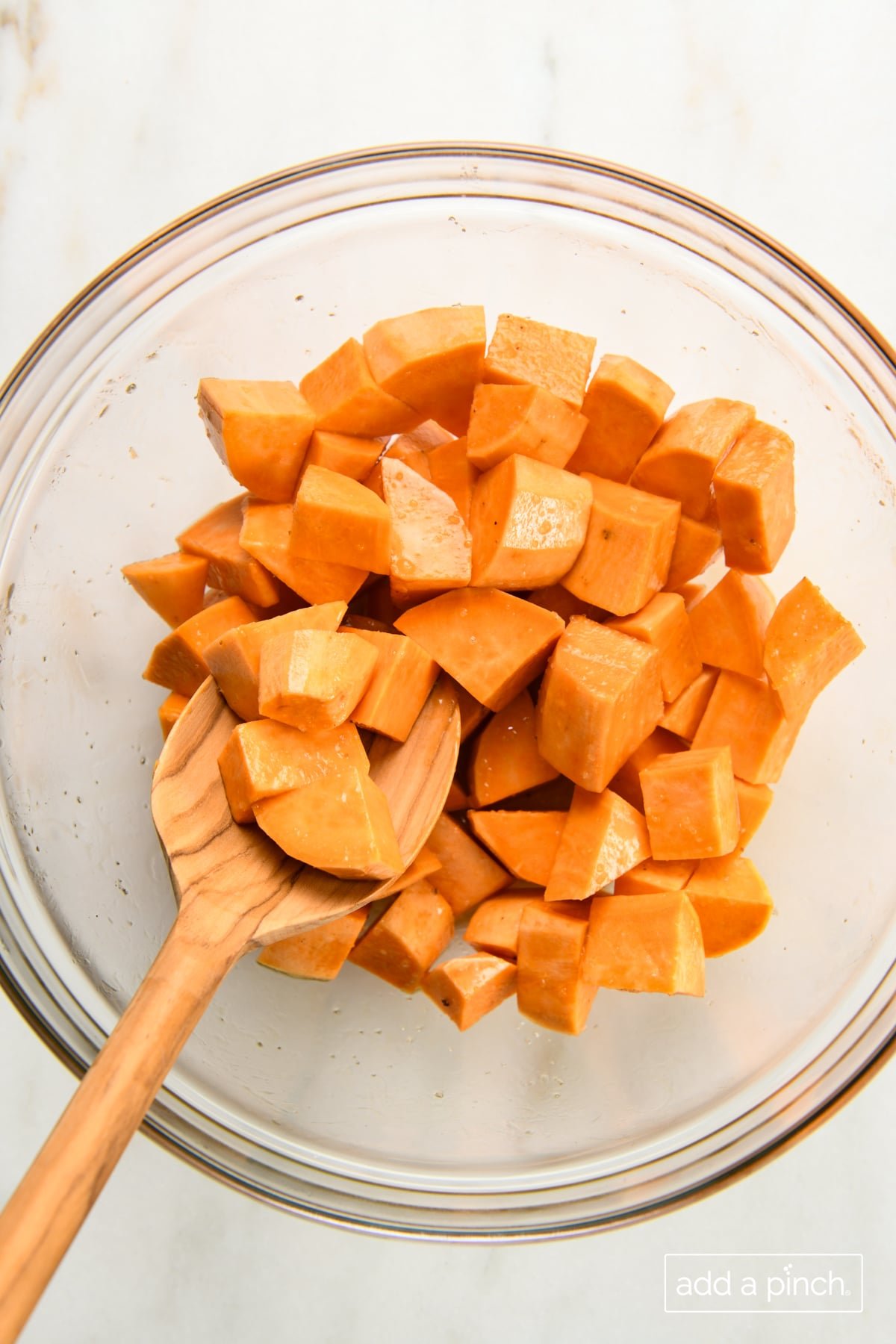 Seasoned sweet potato cubes in a mixing bowl with a wooden spoon.