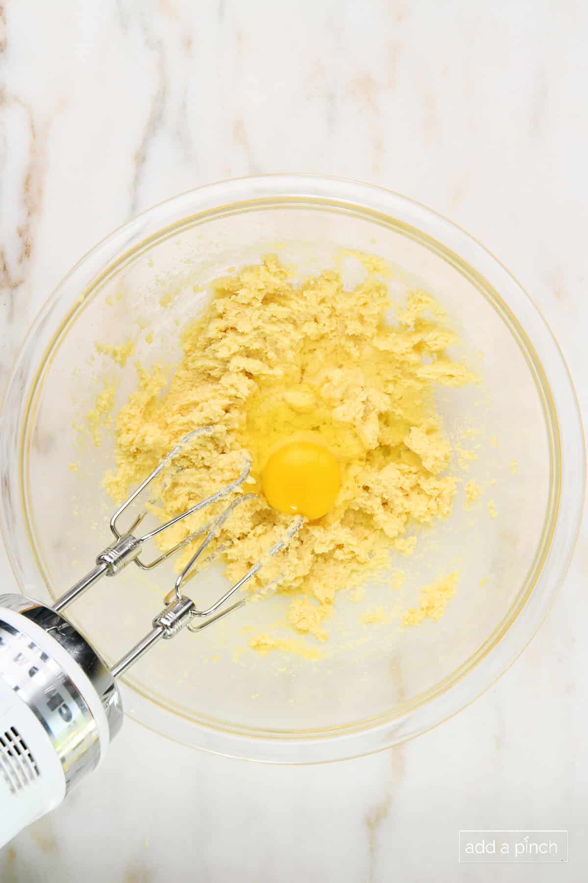 Egg added to butter and sugar mixture in a glass mixing bowl.