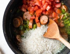 Photo of rice and tomatoes added to sausage and holy trinity cooking for jambalaya.