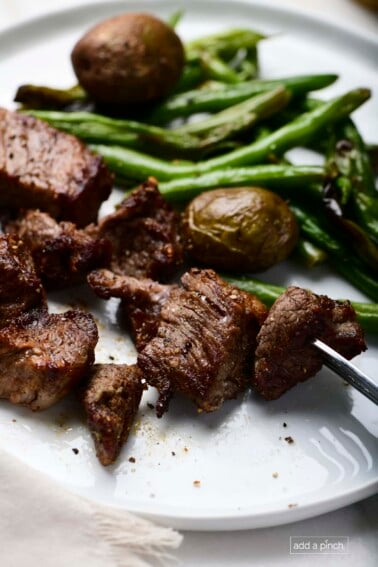 Photo of steak bites served with green beans and potatoes on a white plate.