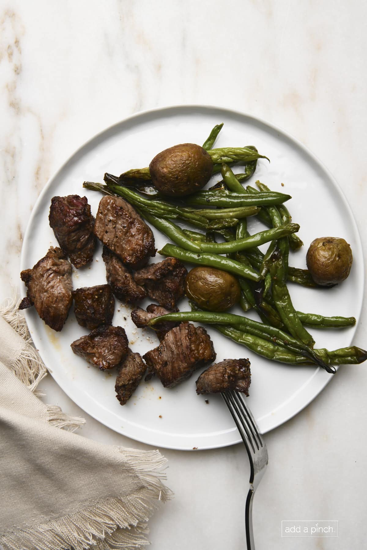 Air Fryer Steak Bites served on a white plate with green beans and potatoes. 