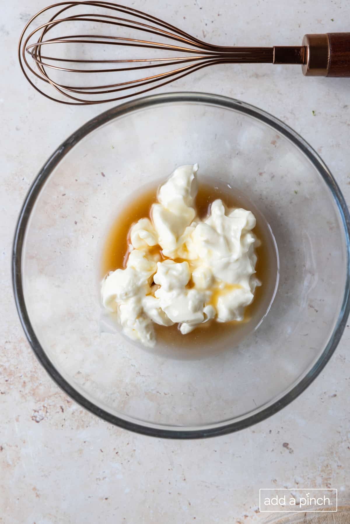 Glass bowl with ingredients for dressing for broccoli salad, along with a whisk.