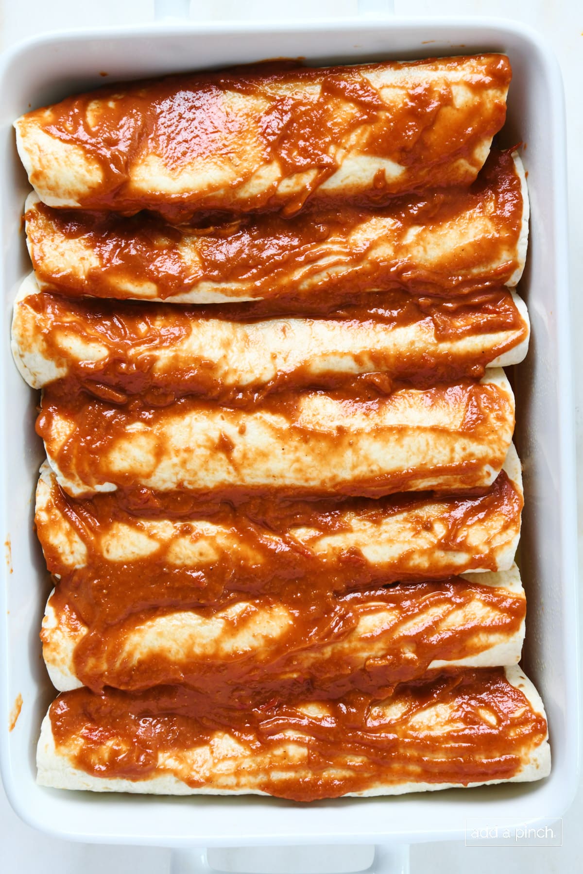 Enchiladas in a white baking dish topped with more enchilada sauce.