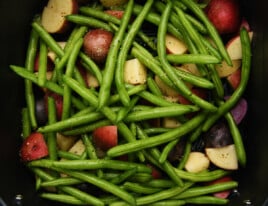 Seasoned green beans and potatoes in air fryer basket.