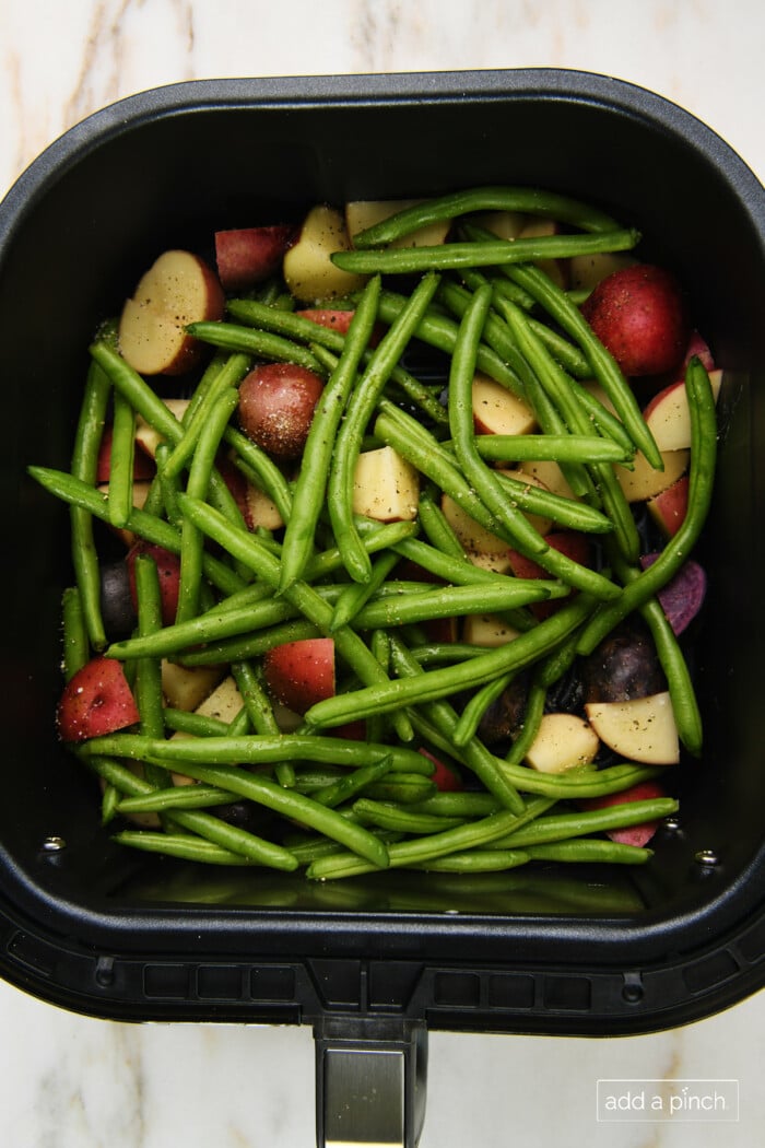 Seasoned green beans and potatoes in air fryer basket.