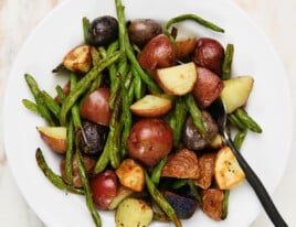 Cooked green beans and potatoes in a white bowl on a marble surface.