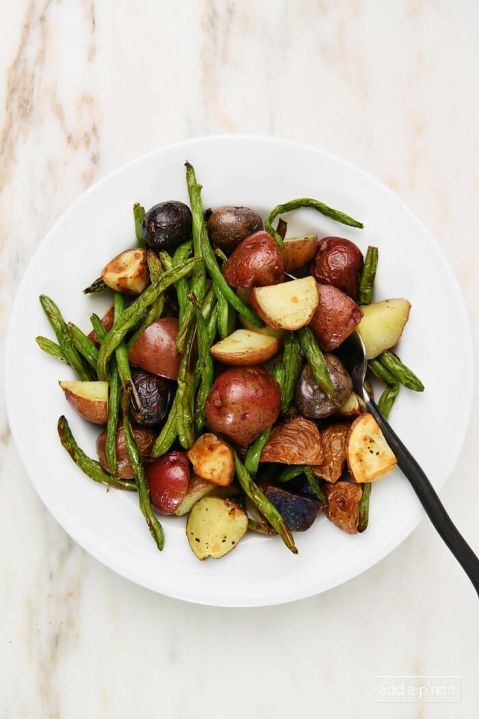 Cooked green beans and potatoes in a white bowl on a marble surface.