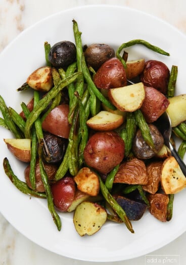 Photo of green beans and potatoes in a white bowl on a marble surface.