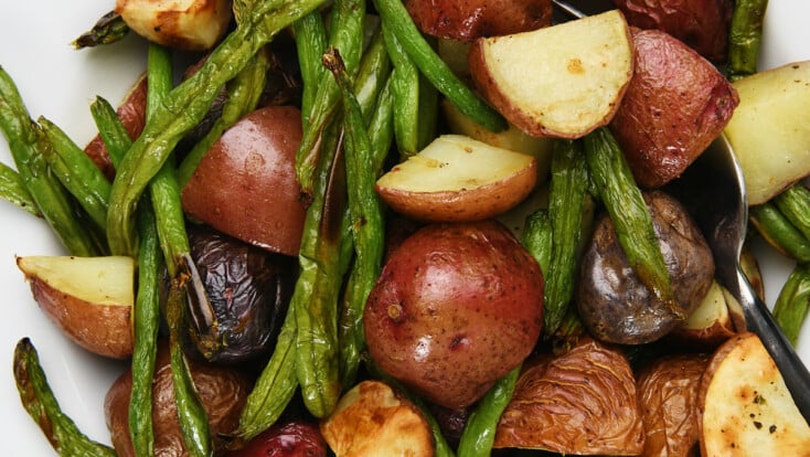 Photo of green beans and potatoes in a white bowl on a marble surface.