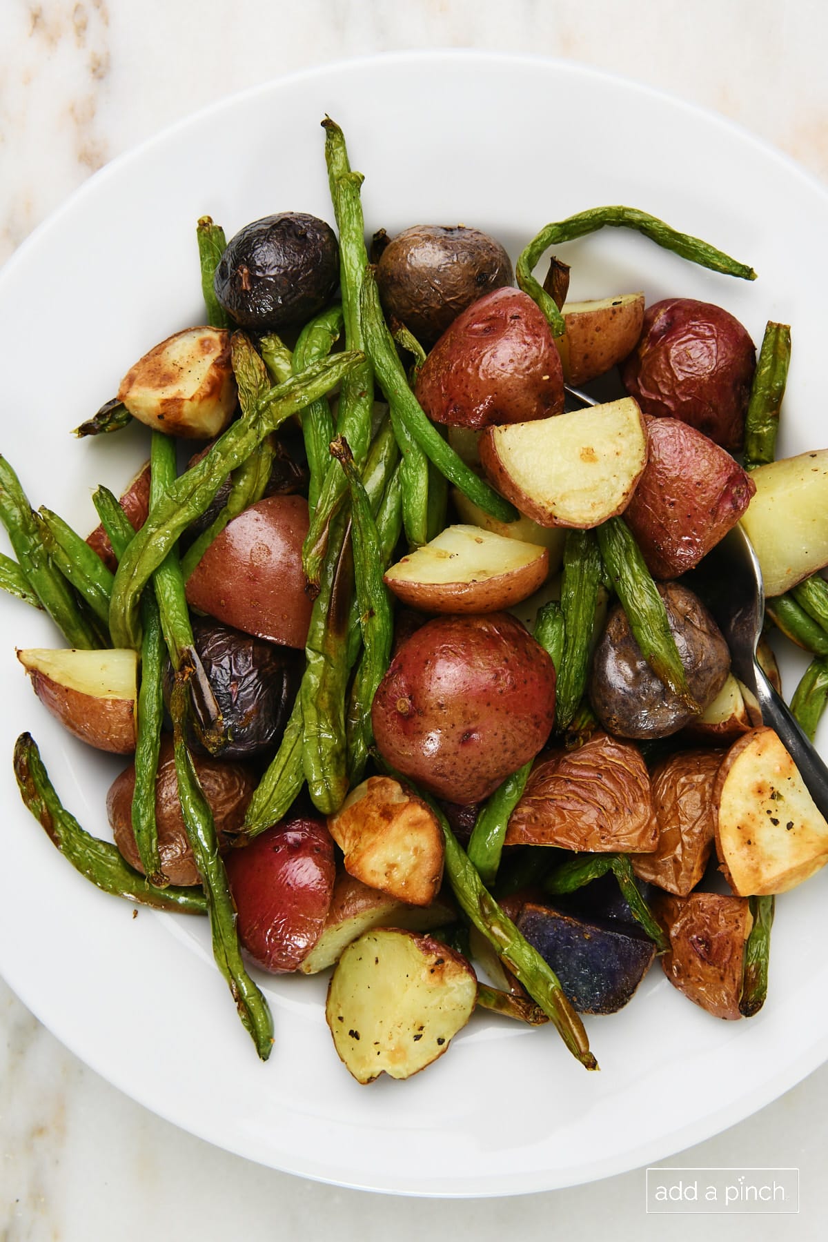 Photo of green beans and potatoes in a white bowl on a marble surface. 