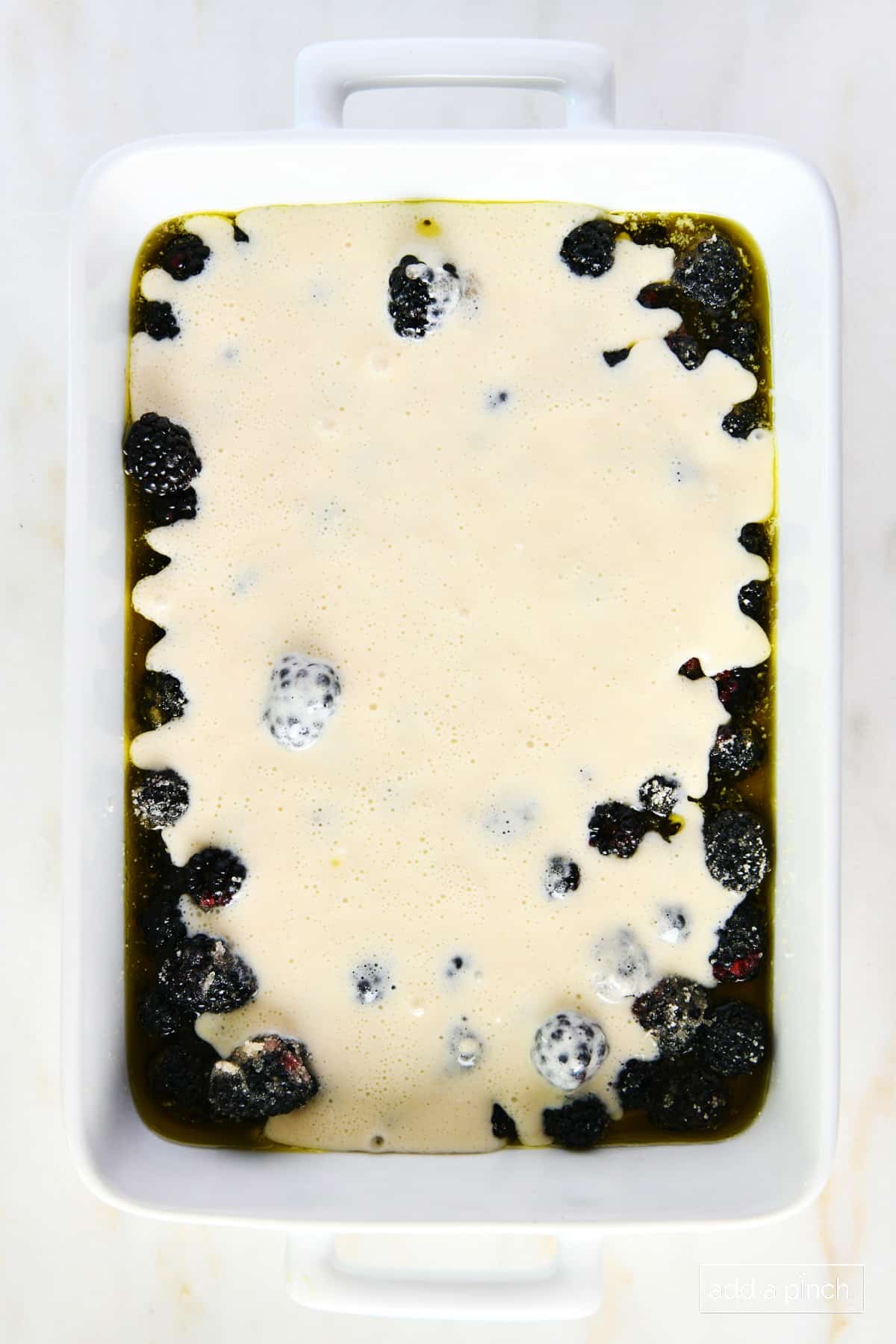 Photo of cobbler batter poured over blackberries and butter.