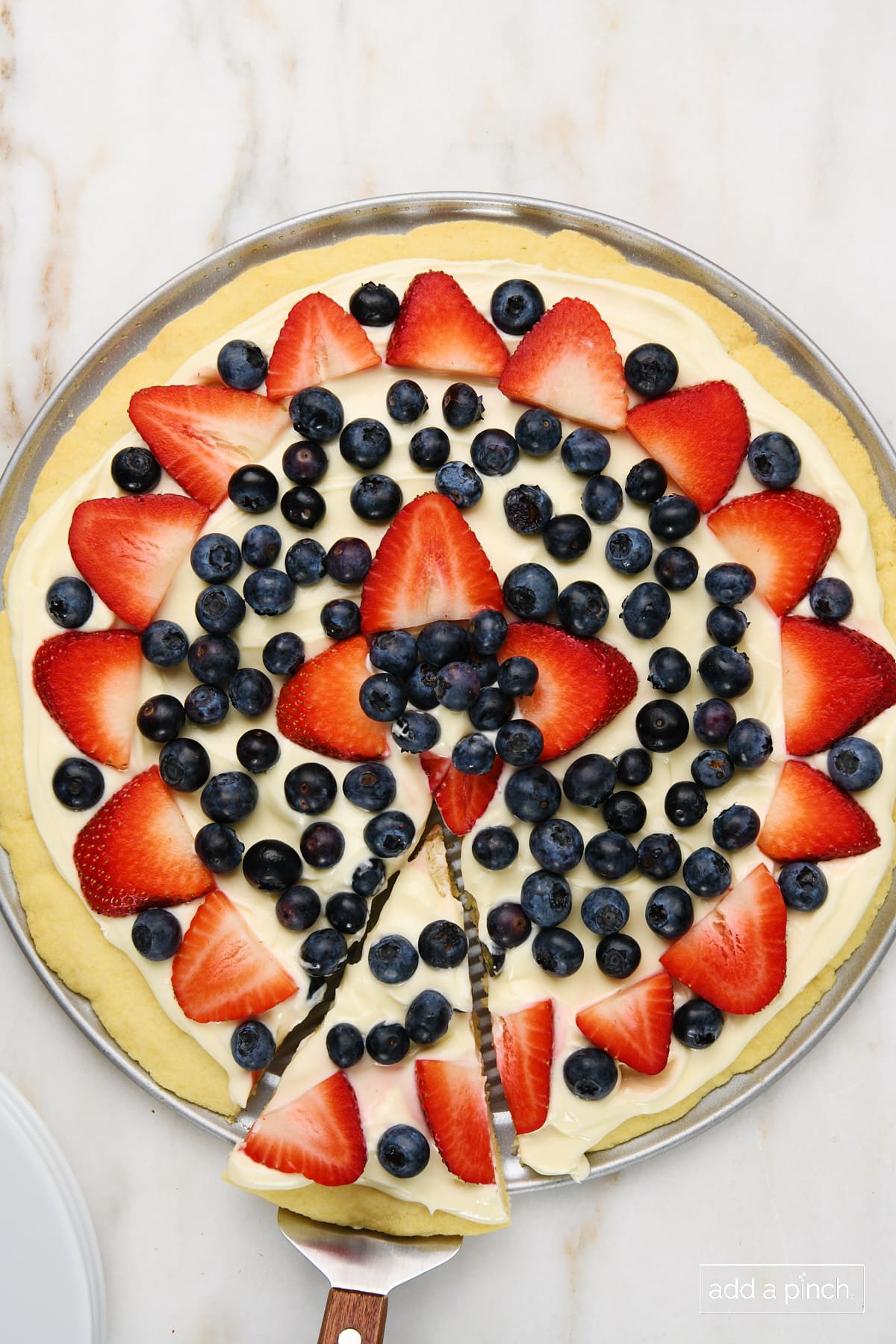 Photo of fruit pizza with a slice for serving.