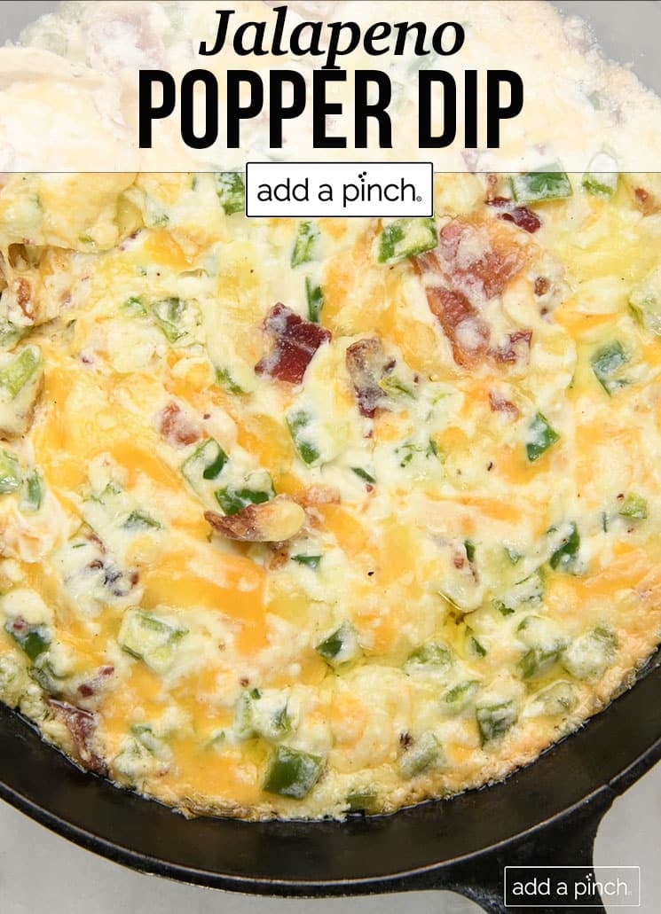 Skillet of dip with cheese, bacon, chopped jalapenos - with text - addapinch.com