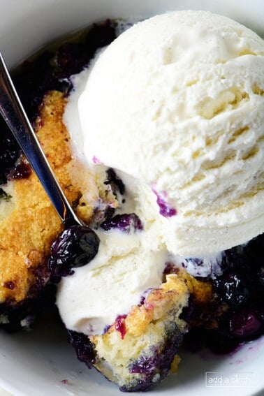Bowl of blueberry cobbler in a white bowl topped with vanilla ice cream.