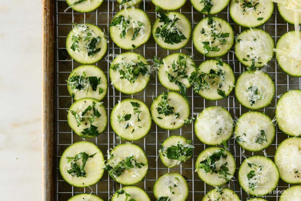 Zucchini Chips sprinkled with Parmesan, chopped parsley and seasoning on a baking sheet ready to place in the oven // addapinch.com