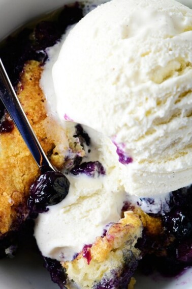 Bowl of blueberry cobbler in a white bowl topped with vanilla ice cream.