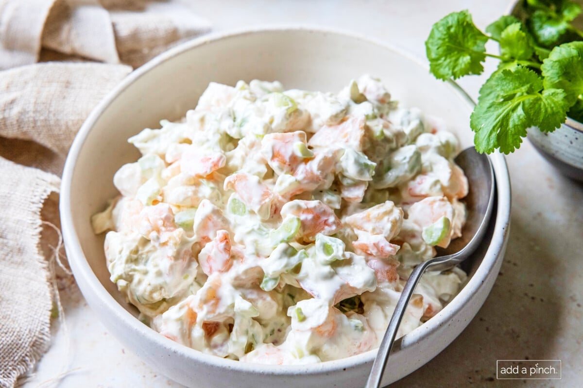 Shrimp dip in a bowl with spoon, surrounded by celery leaves.