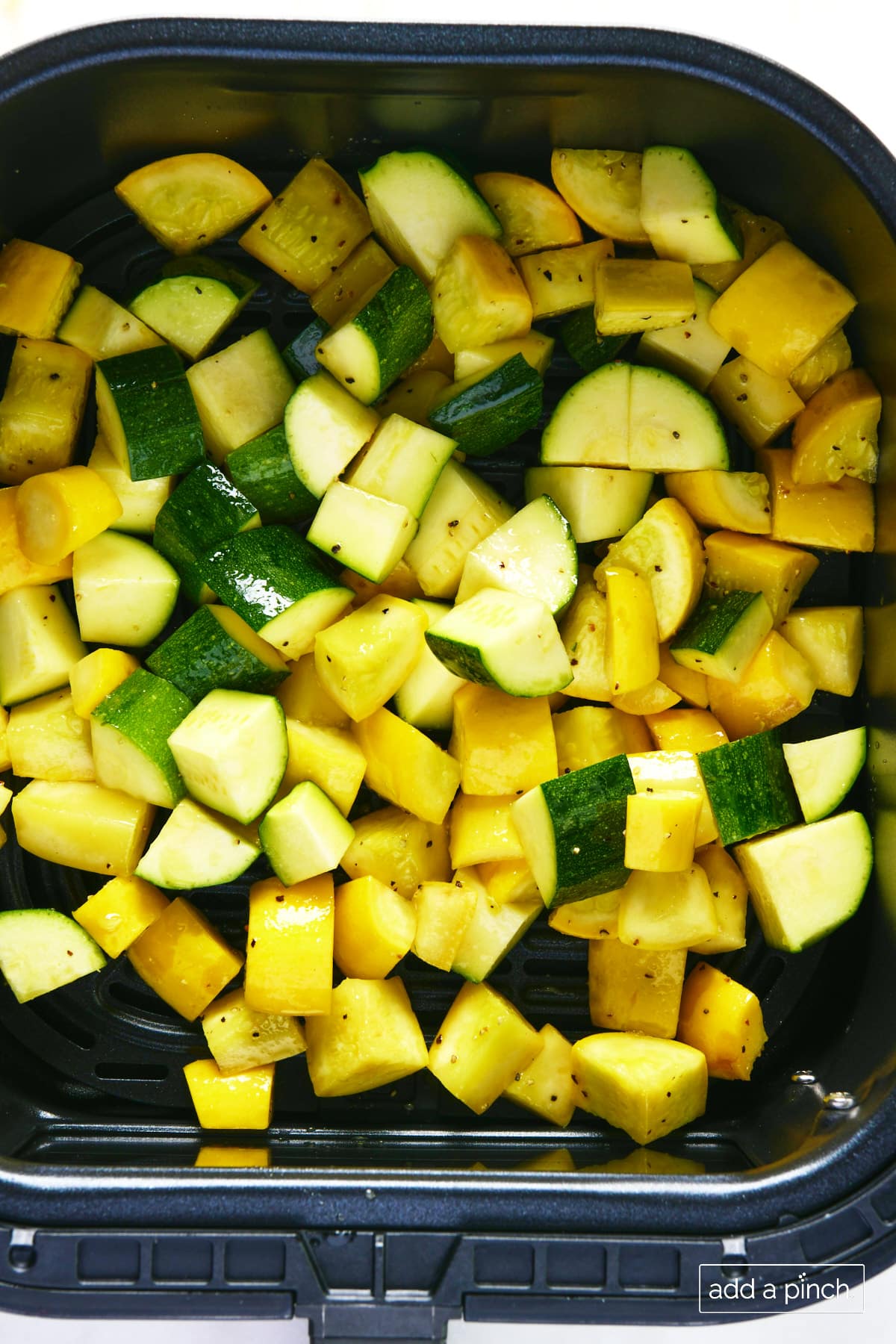 Cut yellow squash and zucchini in an air fryer basket ready to be cooked.