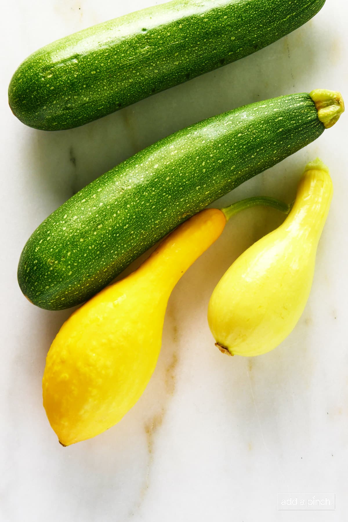 Photo of zucchini and yellow squash on a marble surface.