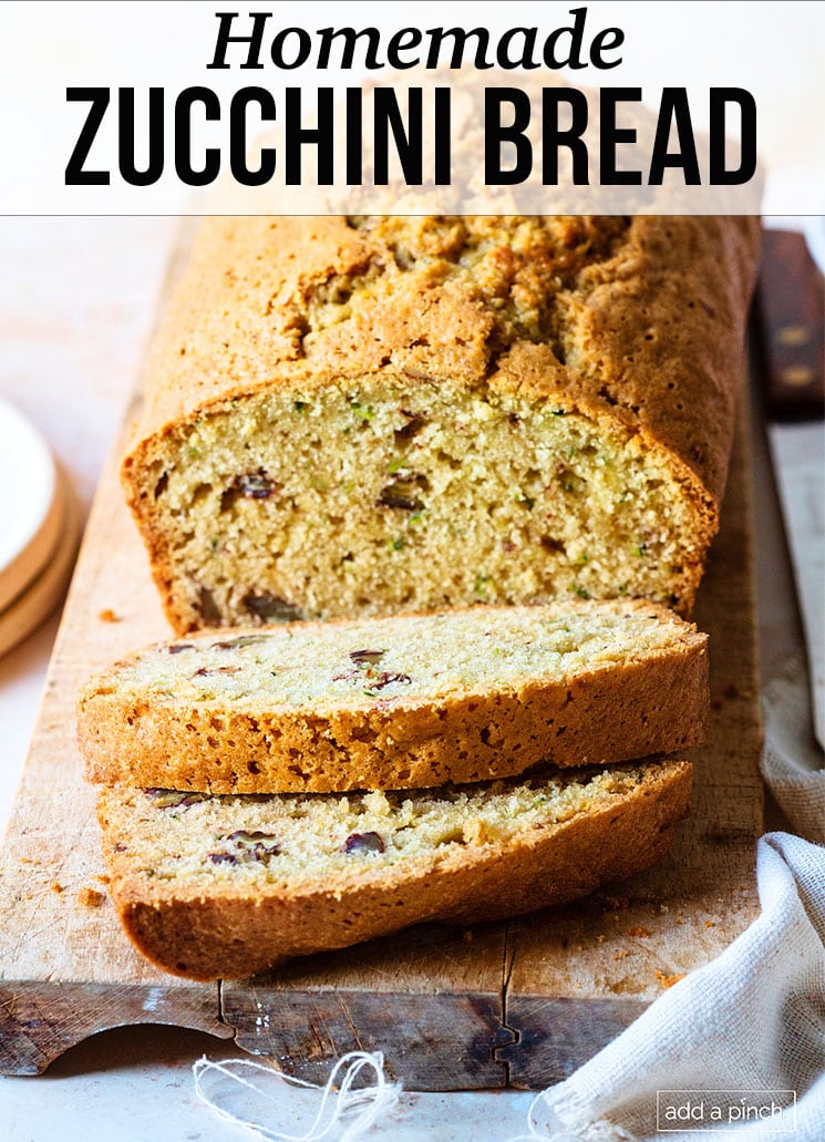 Wooden bread board holds fresh baked zucchini bread that has been sliced - with text - addapinch.com