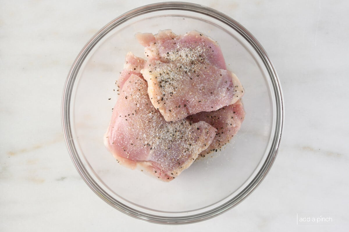Chicken thighs marinating in a glass bowl on a marble surface.