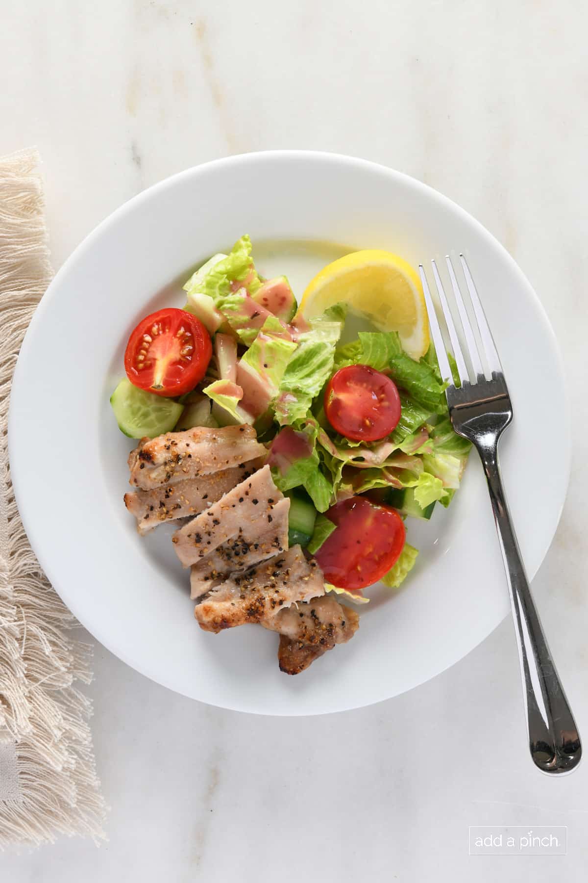 Chicken thighs on a white plate with a salad and lemon.