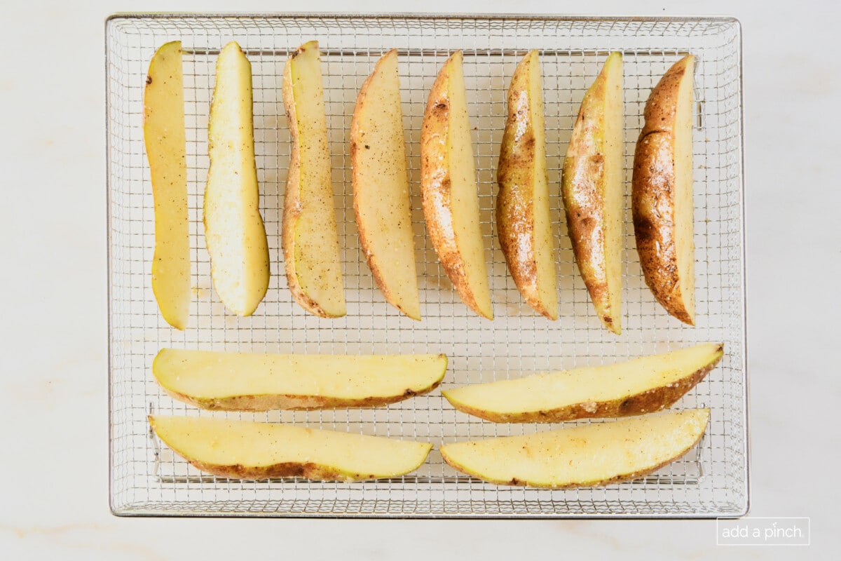 Potato wedges on a metal air fryer basket ready to be cooked.
