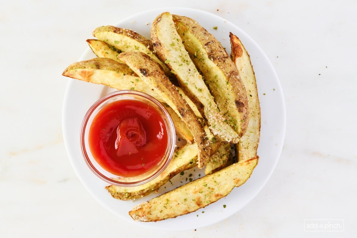 Photo of air fryer potato wedges on a white plate with ketchup.