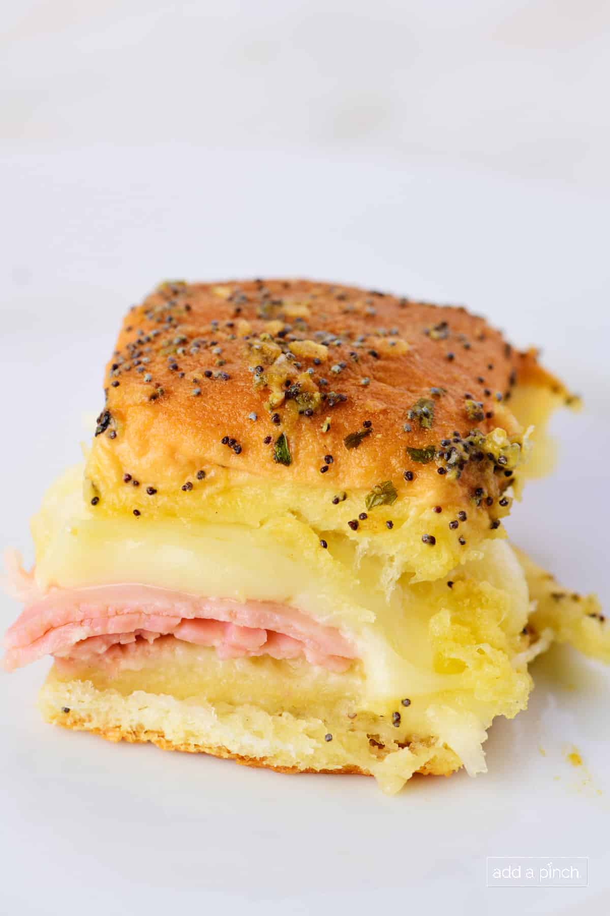 Photo of baked ham and cheese sandwich with poppy seed butter sauce on top.
