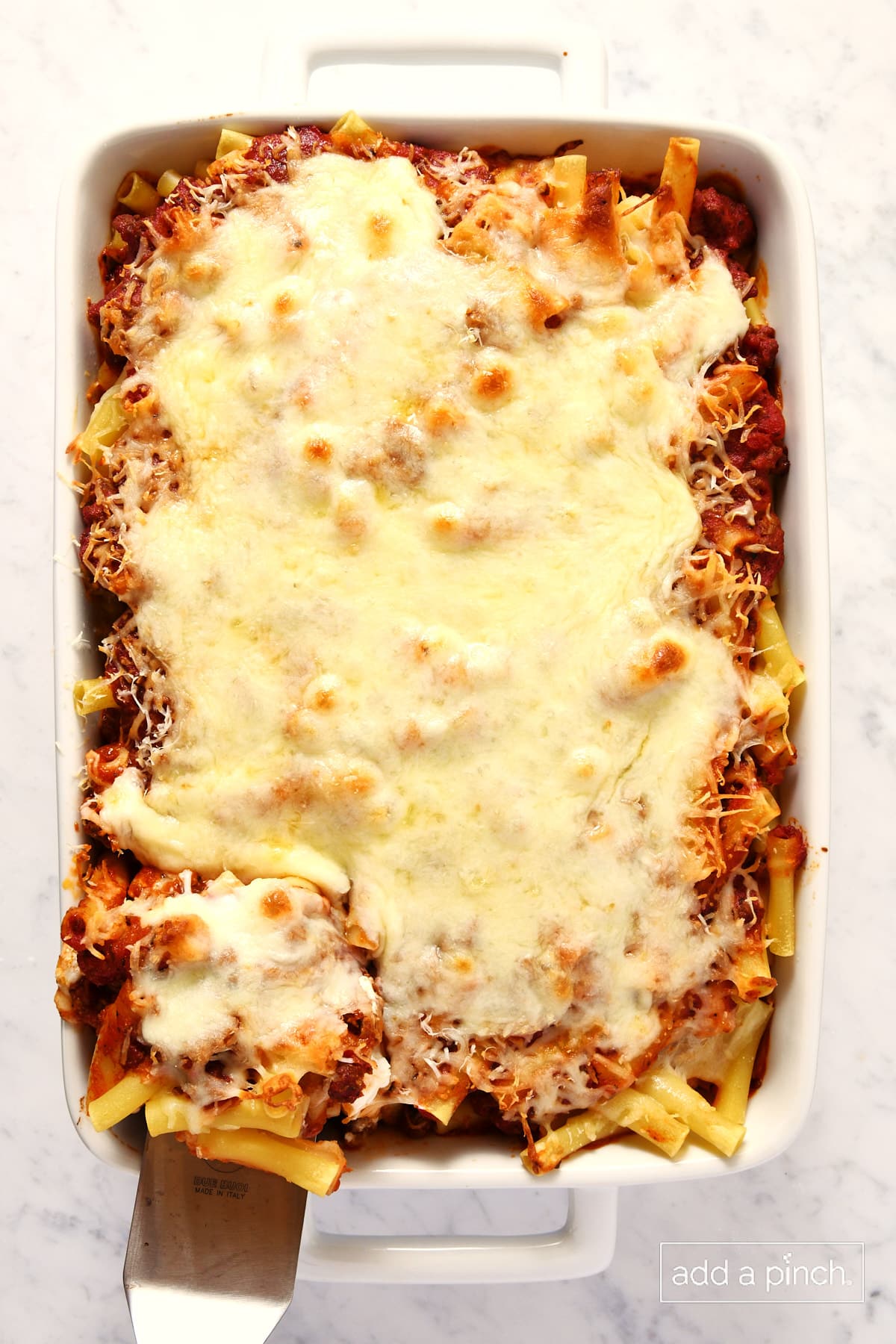 Baked ziti in a baking dish with a serving on a spatula.