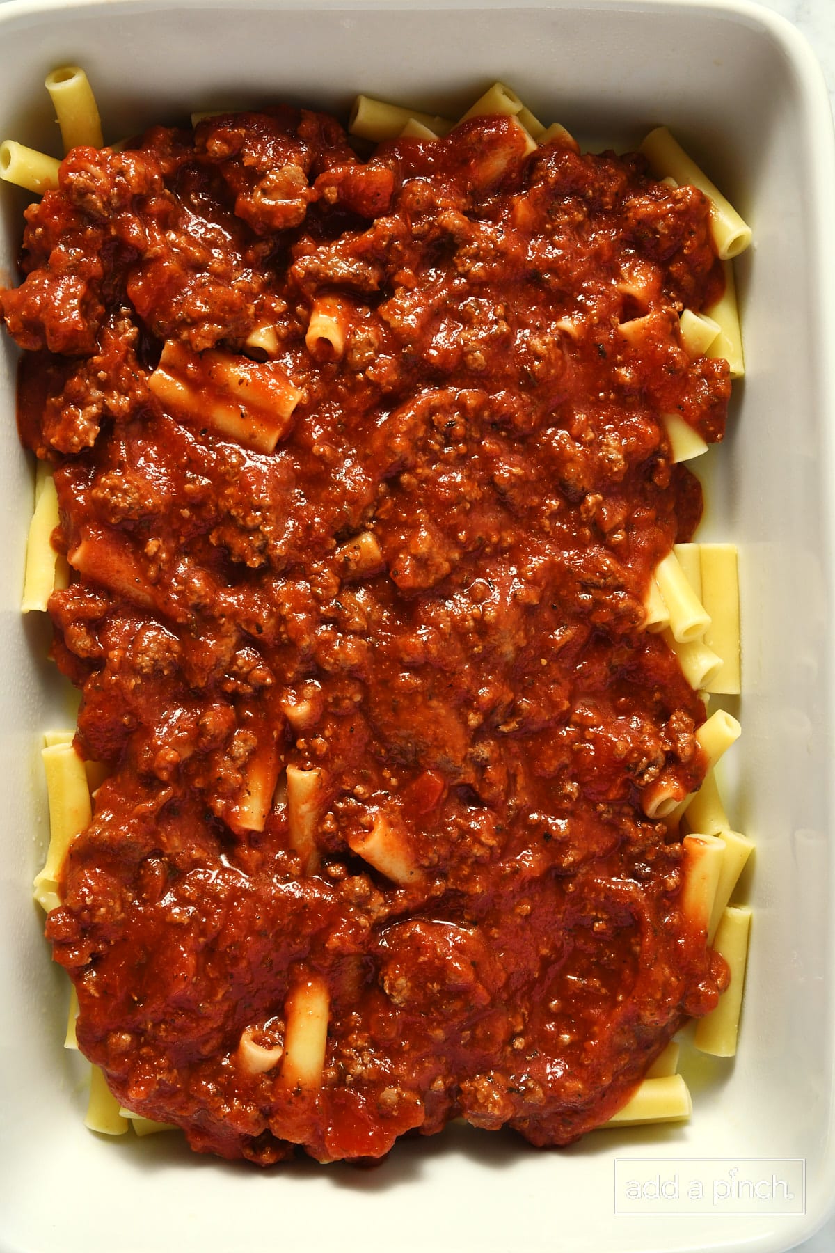 White baking dish with noodles and a layer of meat sauce on top.