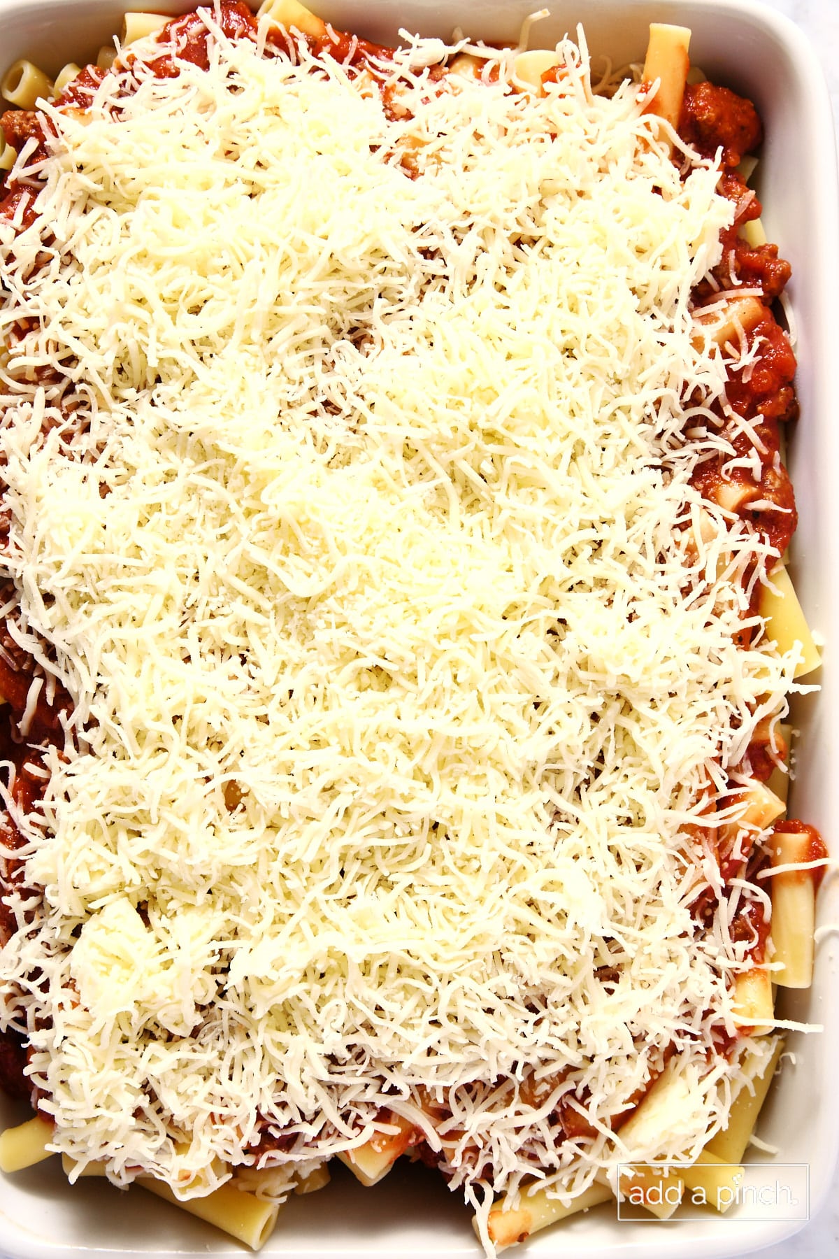 Cheese on top of a noodle and meat sauce layered casserole in a white baking dish.