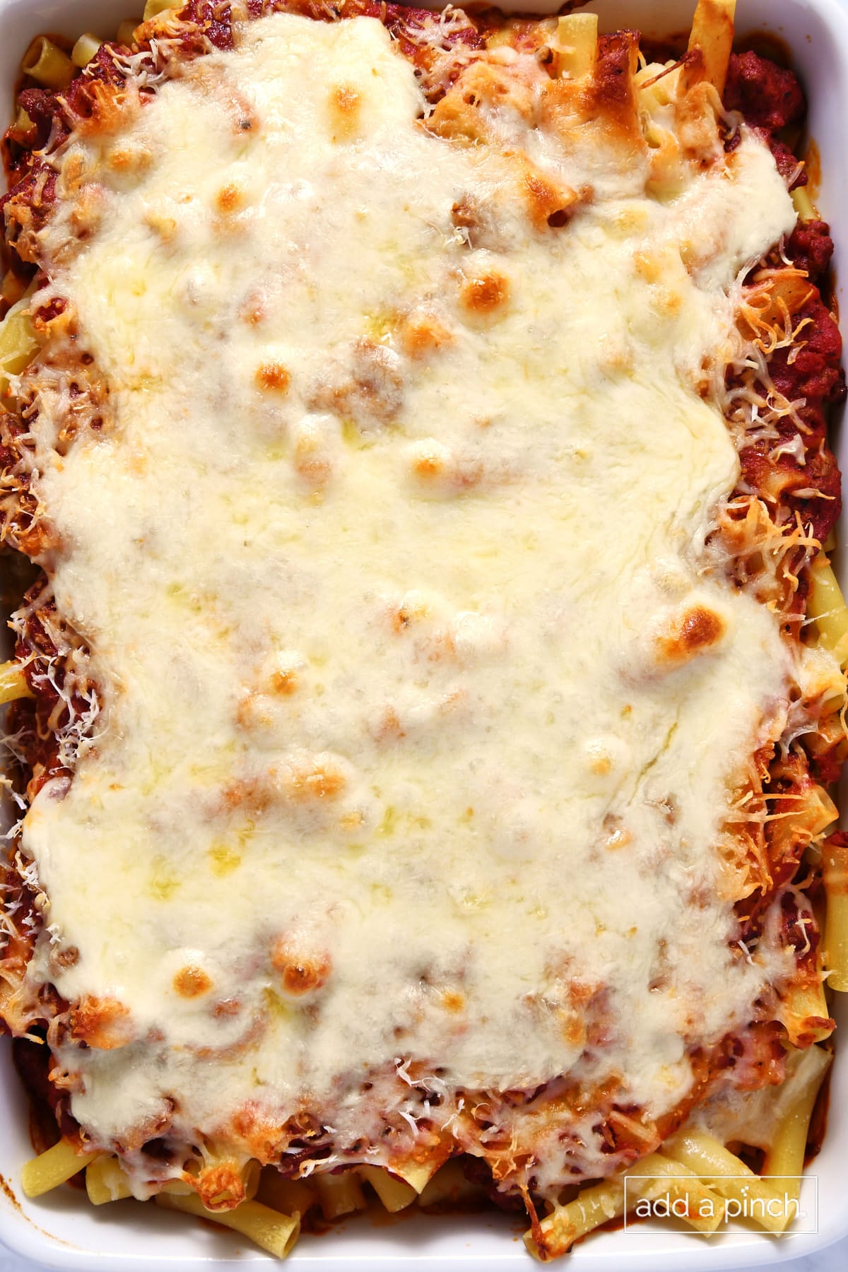 Baked ziti in a white baking dish with melted cheese on top.