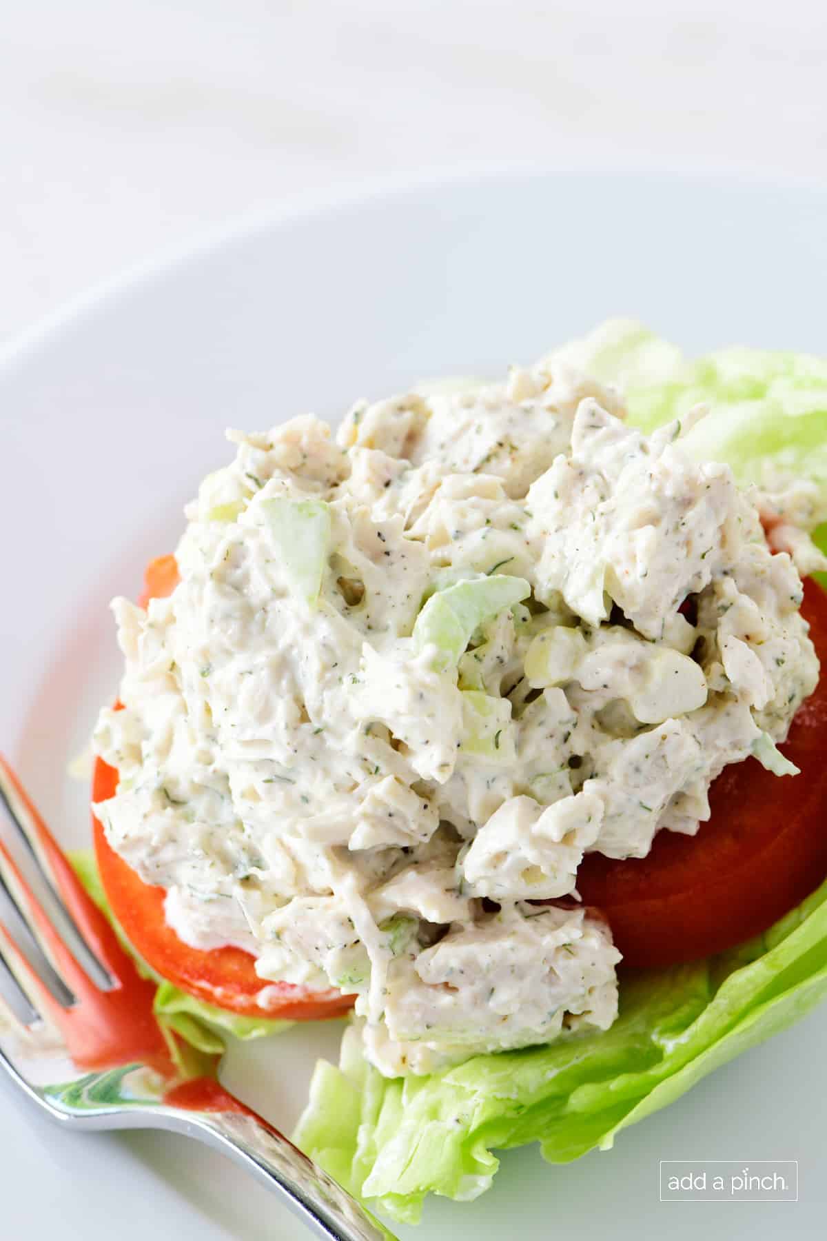 Classic chicken salad on a sliced tomato and lettuce on a white plate.