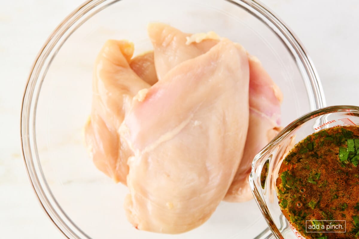 Chicken breasts in a glass mixing bowl with marinade being poured into the bowl.
