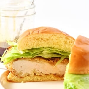 Hot honey chicken sandwich cut in half with jar of hot honey in the background.