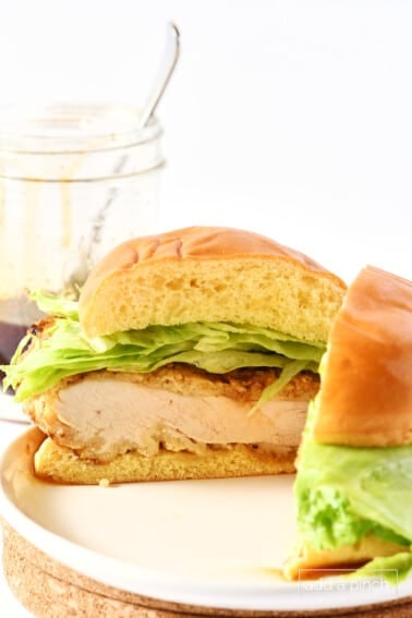 Hot honey chicken sandwich cut in half with jar of hot honey in the background.