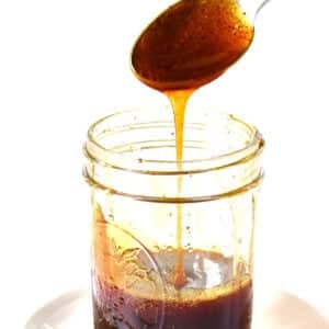 Spoon filled with homemade hot honey drizzling into a jar on a white plate.
