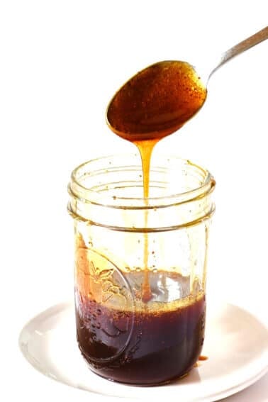 Spoon filled with homemade hot honey drizzling into a jar on a white plate.