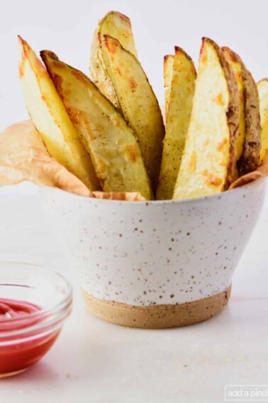 Crispy potato wedges in a pottery bowl with a ramekin of ketchup.