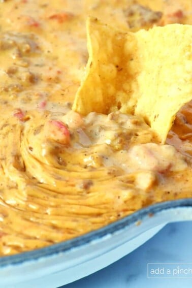 Tortilla chip dipped into Rotel Dip in a white skillet.