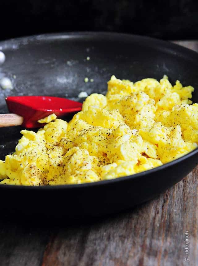 Skillet with fluffy scrambled eggs sprinkled with pepper, stirred with a silicone spatula - addapinch.com