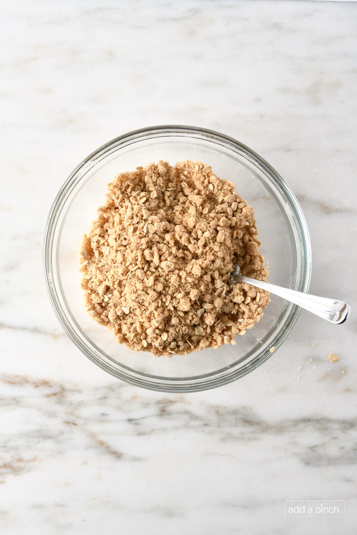 Oat topping for apple crisp in a glass bowl on a marble countertop.